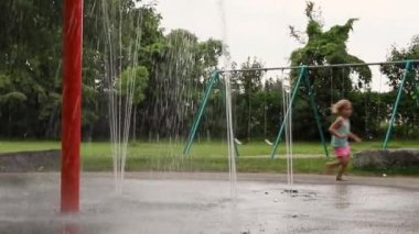 Yerel halk parkında çeşmeler ve çalışan çocuklar. Yaz günü çocuk parkında sıçrama tahtası ve salıncaklar..