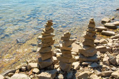 Taş cairn taş sanatı mavi bir su akan göl yakınında bir taş üzerinde dengelenir. Gölde güneşli bir gün. Doğayla uyum ve sakinlik havası..