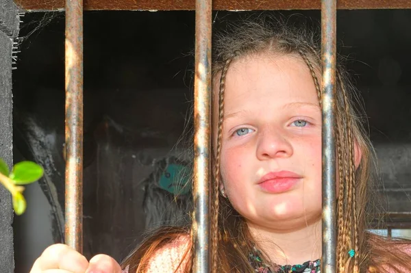 Foto de uma menina segurando bares. Rapariga triste atrás das barras de ferro. Uma menina atrás das grades. Conceito de violência — Fotografia de Stock