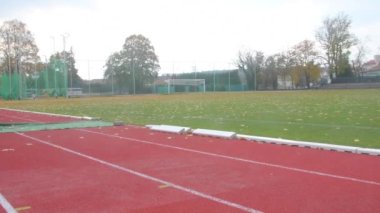 Sonbaharda atletizm stadyumunda kırmızı koşu pisti. Sonbaharda terk edilmiş atletizm pisti. Futbol sahasında panoramik manzara. Bitmiş atletizm ve futbol sezonu kavramı