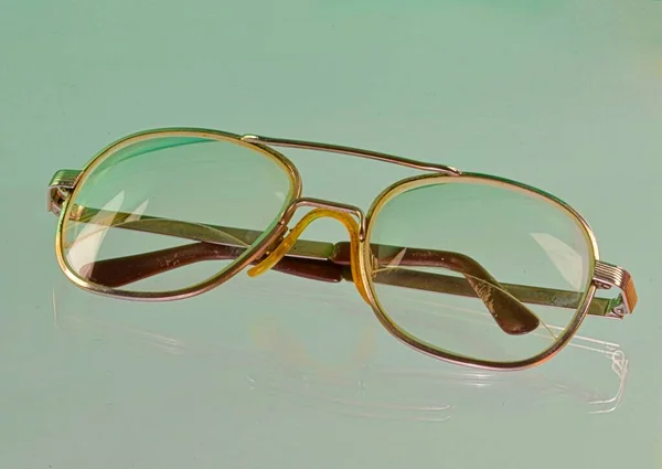 Reflectie van de bril. Gouden brillen, close-up. Een bril. Oude stijl brillen. Bril met transparante lenzen. Vintage Bril op gereflecteerde achtergrond. Sluiten van versleten brillen — Stockfoto