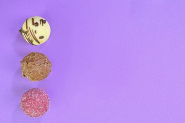 Çikolatalı bonbonlar ya da eflatun kaplama pralinler. Fotokopi alanı olan eflatun arkaplanlı çikolatalı pralinler. Düz yatış, üst görünüm.