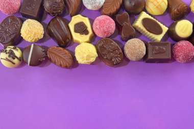 Chocolate pralines frame top view stock images. Chocolate candies on a lilac background. Chocolate frame top view. Chocolate pralines background with copy space for text. Border of different candies.