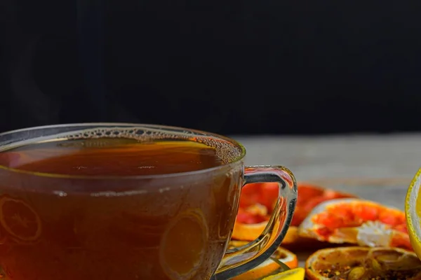 熱いお茶と黒の蒸気でカップ シナモンスティック アニススター レモンと白の木製のテーブルの背景にドライフルーツと紅茶のガラスカップ マクロイメージ — ストック写真