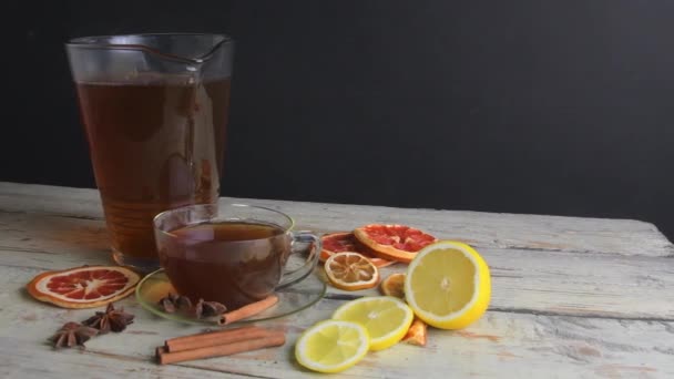 Varmt te i glas tekanna och kopp med ånga på trä skrivbord svart bakgrund — Stockvideo