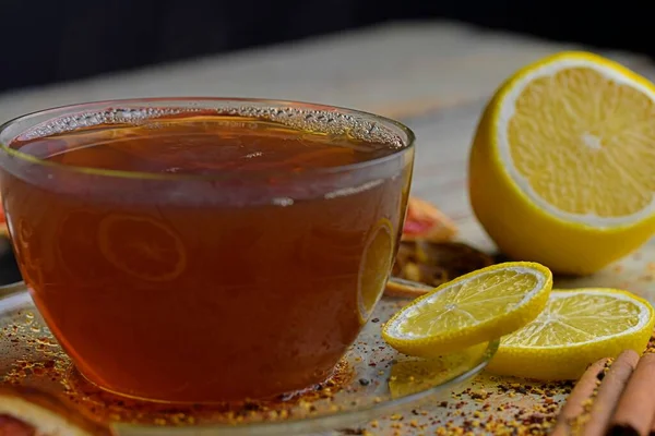 Sıcak çay ve siyah buharlı bir fincan. Tarçın çubuklu bir bardak siyah çay, anason yıldızı, limon ve kuru meyve beyaz tahta masa arkasında. Makro resim — Stok fotoğraf