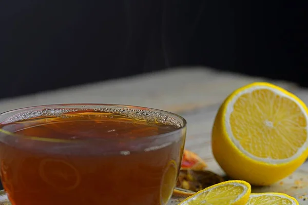 Ahşap masa arkasında tarçın çubukları olan bir bardak çay. Tarçın çubukları, yıldız anason, limon ve kurutulmuş meyve. Siyah arka plan. Makro görüntü. Hayat konsepti. — Stok fotoğraf