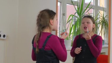 Evde makyajla oynayan sevimli küçük bir kız. Mutlu çocuk evde annesinin kozmetik ürünleriyle deney yapıyor. Kızın ayna yansıması.