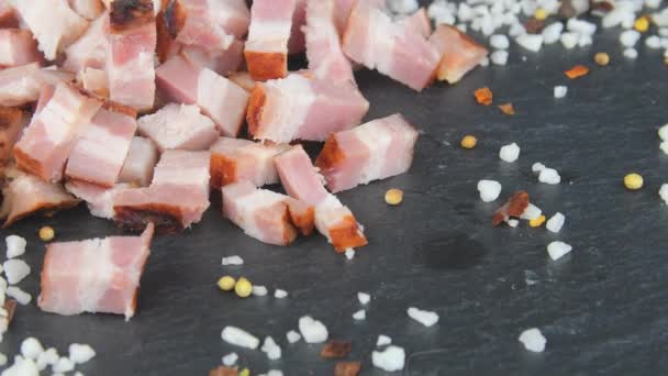 Délice de viande. Cubes de bacon tranchés, basilic et assaisonnements sur un plateau rotatif en ardoise. Macro — Video