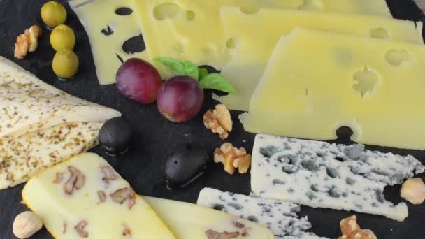 Piatto di formaggio con formaggi assortiti, uva, noci su fondo nero, spazio per la copia. Formaggio italiano e piatto di frutta con miele e ardesia di sfondo rotante — Video Stock