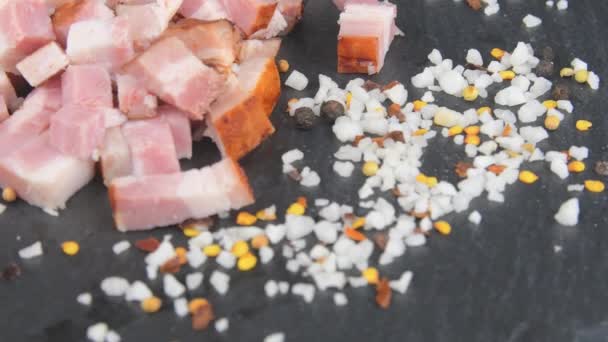 Meat delicacy. Sliced bacon cubes, basil and seasonings on a rotating slate tray. Macro — Stock Video