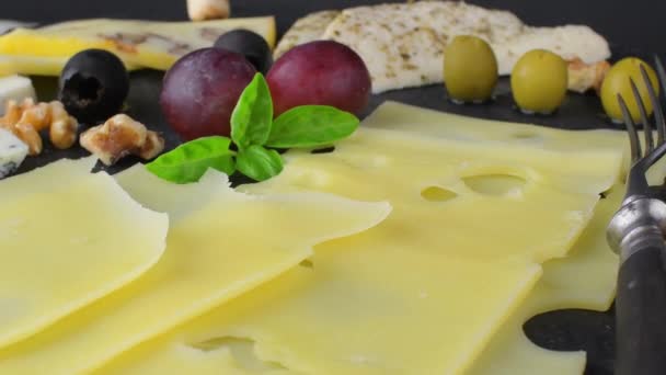 Piatto di formaggio. Emmental, formaggio Camembert, formaggio blu, bastoncini di pane, noci, nocciole, uva su vassoio di ardesia rotante — Video Stock