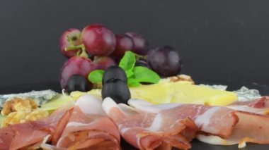 Siyah tahtada çeşitli peynirler var. Brie peyniri, çedar dilimleri, ceviz, üzüm, zeytin ve Schwarzwald jambonu. Yine de hayat yemeği. Uzayı kopyala Dönen tepsi