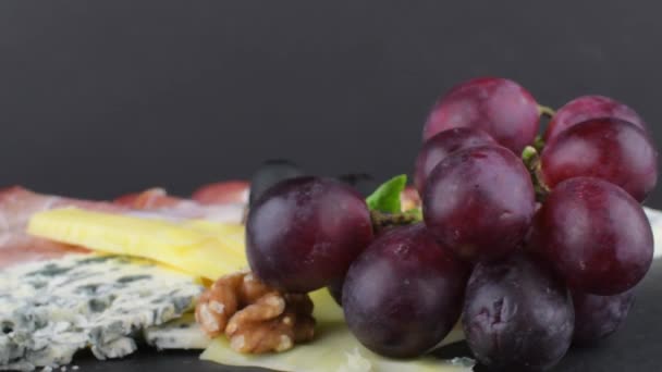 Vassoio con prosciutto di Schwarzwald, formaggi, noci, olive nere. Decorato con basilico. Cibo sul backgroud ardesia. Copia spazio — Video Stock