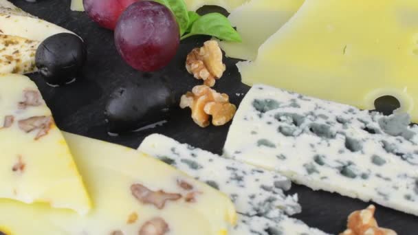 Piatto di formaggio. Emmental, formaggio Camembert, formaggio blu, bastoncini di pane, noci, uva nocciole su vassoio di ardesia rotante — Video Stock