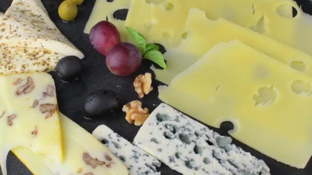 Bandeja de queso con quesos variados, uvas, frutos secos sobre fondo negro. Bandeja italiana de queso y fruta sobre fondo giratorio de pizarra — Vídeos de Stock
