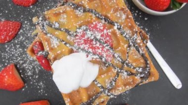 Yaban mersinli waffle, çilek, erimiş çikolata ve üstüne krema. Siyah arka planda böğürtlenli Belçika waffle 'ı ve pudra şekeri. Dönen arkaplan
