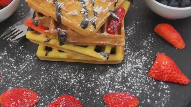 Belgian waffles for breakfast or brunch with fresh blueberries, strawberries, melted chocolate and whipped cream on top. Rotating stack of waffles — Stock Video