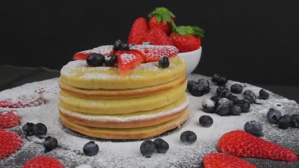 Frittelle con bacche di frutta su sfondo nero. Mirtilli, fragole e zucchero a velo sui pancake. Cibo a rotazione. Copia spazio — Video Stock