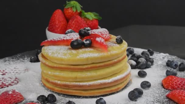 Panqueques con bayas y azúcar glaseado para el desayuno sobre un fondo negro. Copiar espacio. Panqueques giratorios — Vídeo de stock