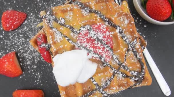 Gaufres belges carrées aux baies, chocolat fondu et sucre glace sur une assiette noire. Gaufres sucrées sucrées savoureuses. Fond tournant — Video