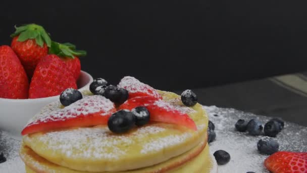 Colazione estiva salutare, pancake americani classici fatti in casa con bacche fresche e zucchero a velo. Fondo nero. Copia spazio — Video Stock