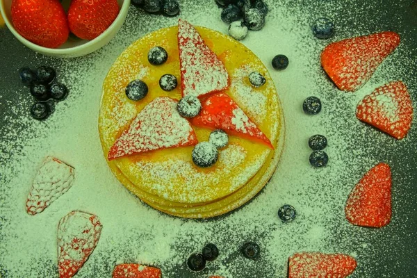 Pancake dengan buah beri di latar belakang hitam. Pancake segar. Blueberry, stroberi dan gula icing pada pancake. Letak rata — Stok Foto