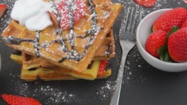 Meyveli Belçika waffle 'ları, erimiş çikolata ve siyah tabakta krema şekeri. Tatlı, tatlı waffle 'lar. Dönen arkaplan