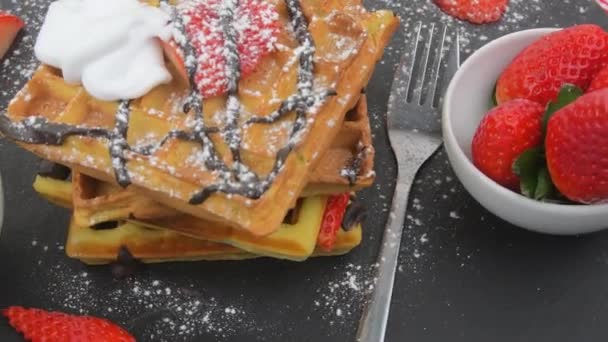 Gaufres belges carrées aux baies, chocolat fondu et sucre glace sur une assiette noire. Gaufres sucrées sucrées savoureuses. Fond tournant — Video