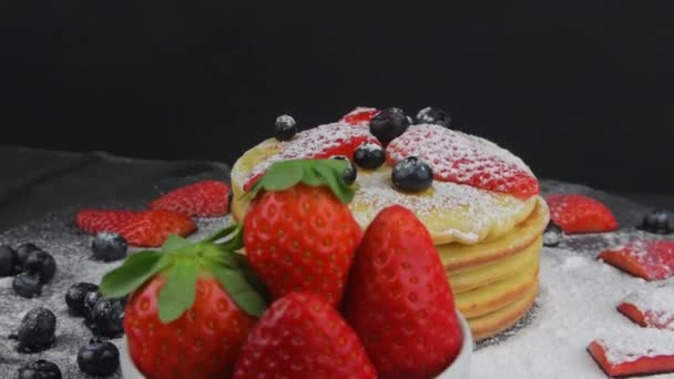 Panqueques con bayas y azúcar glaseado para el desayuno sobre un fondo negro. Copiar espacio. Panqueques giratorios — Vídeos de Stock