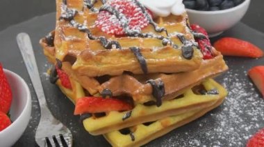 Meyveli Belçika waffle 'ları, erimiş çikolata ve siyah tabakta krema şekeri. Tatlı, tatlı waffle 'lar. Dönen arkaplan