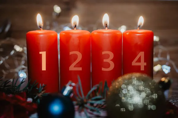 Four numbered red advent candles with first candle lit and christmas decoration lying in snow as template