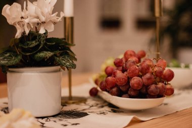 Red grapes on a white plate on a decorated holiday table next to a flower in a pot.