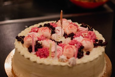 Birthday cake with pink whipped cream flowers and candles.