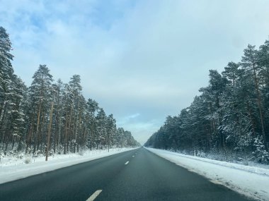 Asfalt yolu, orman ve mavi gökyüzü olan güzel kış manzarası. Donmuş kış günü ve yol sürücüsü.