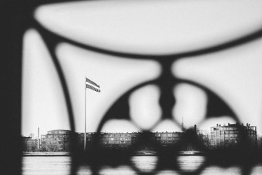 Riga, Letonya - 16-03-2022: Riga, Letonya bayrağıyla Daugava nehrinin kıyısında, Letonya 'da bulutlu bir günde