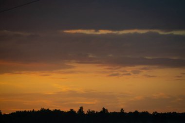 ağaçlar ve alanlar üzerinde gökyüzünde dramatik kırmızı günbatımı renkleri. Letonya yaz günbatımı
