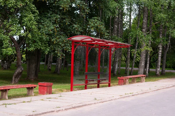 Empty red public transport stop in summer. Self isolation. Bus and minibus stops. Glass stop with bench and waste bin. Stop without people, without passengers. bus stop sign