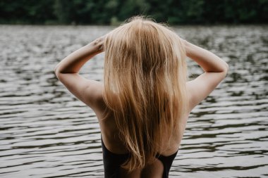 Suda duran ve yüzmeden önce saçını düzelten genç ve güzel bir kadın. Sıcak yaz akşamı.