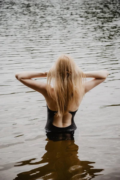 Suda duran ve yüzmeden önce saçını düzelten genç ve güzel bir kadın. Sıcak yaz akşamı.