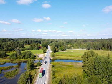 Drone shot. Aero photography with a highway over a river on which heavy transport and everyday cars move. The highway seems to go into the distance through the forest.