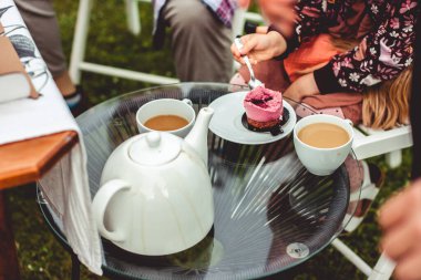 Kadın, güzel bir cam masanın üzerinde duran çikolata tabanlı ve menekşe kremalı bir kekin tadını çıkarıyor. Yanında beyaz bir kahve fincanı var..