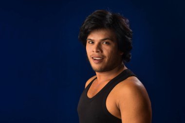 Portrait of a young man posing and showing his muscular body. The concept of a healthy lifestyle on blue background.