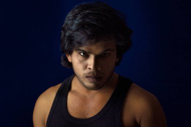 Portrait of a young man posing and showing his muscular body. The concept of a healthy lifestyle on blue background.