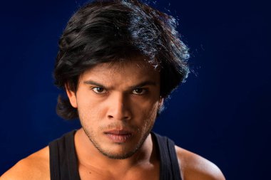 Portrait of a young man posing and showing his muscular body. The concept of a healthy lifestyle on blue background.