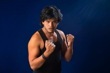 Portrait of a young man posing and showing his muscular body. The concept of a healthy lifestyle on blue background.