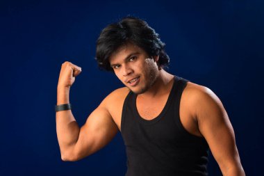 Portrait of a young man posing and showing his muscular body. The concept of a healthy lifestyle on blue background.