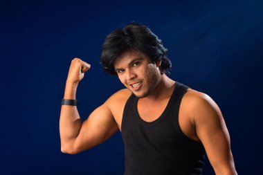 Portrait of a young man posing and showing his muscular body. The concept of a healthy lifestyle on blue background.