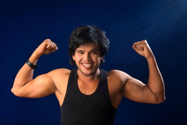 Portrait of a young man posing and showing his muscular body. The concept of a healthy lifestyle on blue background.