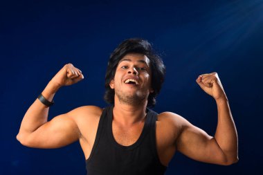 Portrait of a young man posing and showing his muscular body. The concept of a healthy lifestyle on blue background.